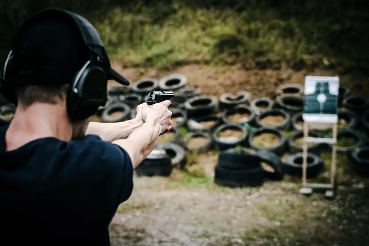 Adult male practicing target shooting outdoors with pistol at a range