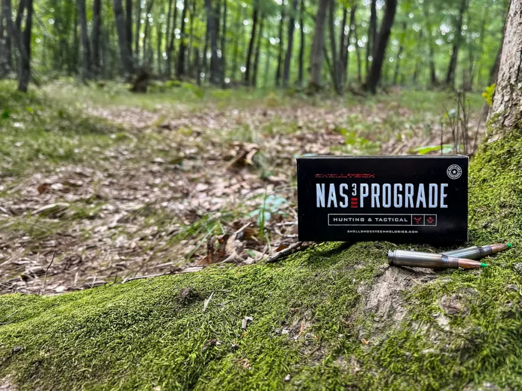 A box of Shell Tech 308 NAS³ PROGRADE with two loaded bullets in green forest